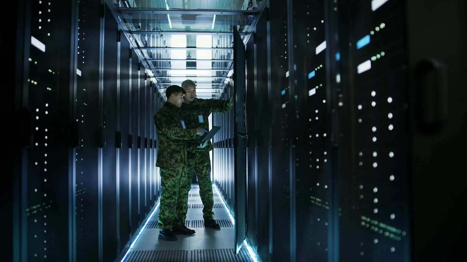 Two service members working in a data center aisle between server racks