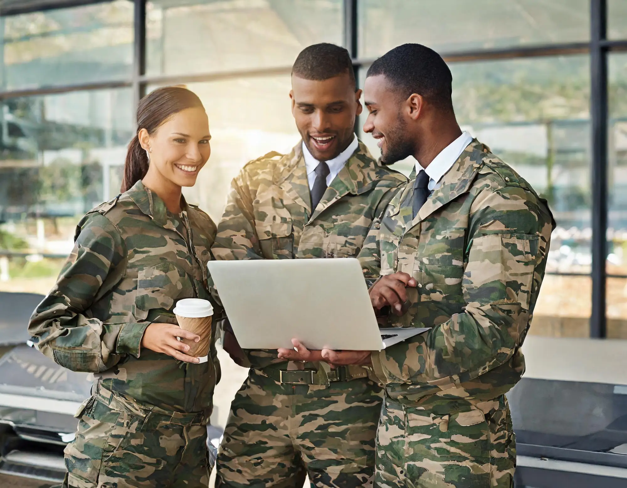 Three colleagues, two in military uniform, reviewing work on a laptop